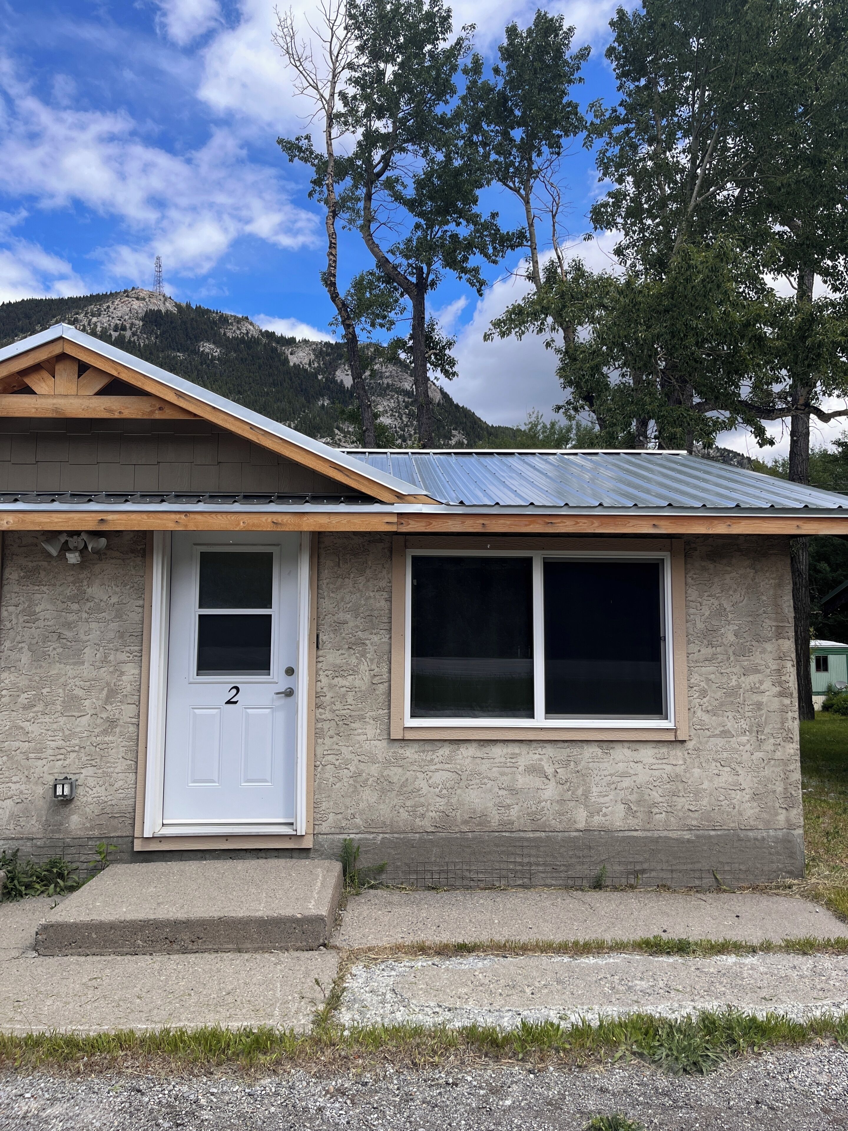 Una casa de un piso con puerta y ventanas blancas, techo de metal inclinado y fachada de piedra.