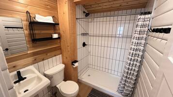 A bathroom with a wooden ceiling, white tiled walls, a white sink, a toilet, and a shower with a striped curtain.