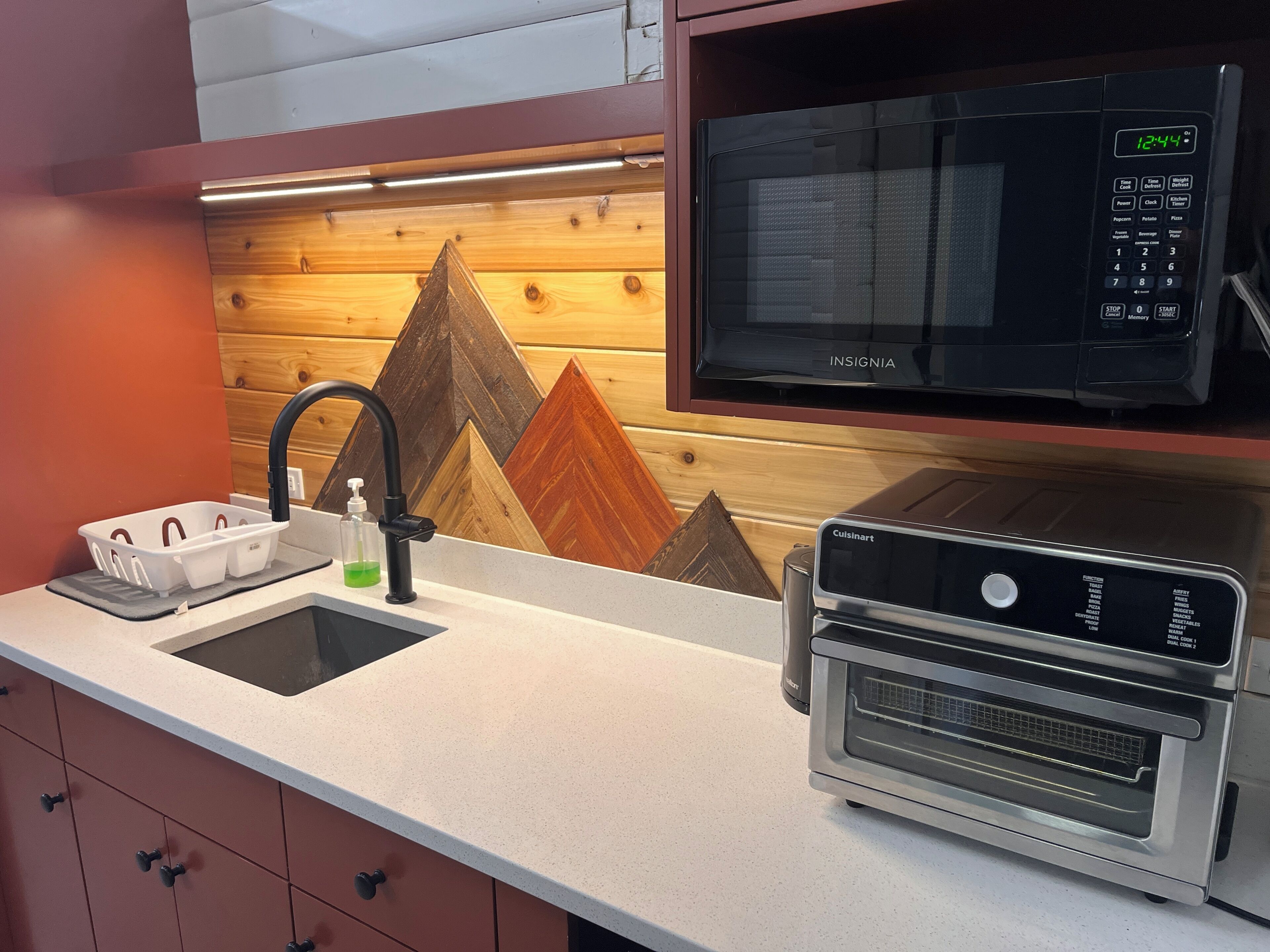 Una cocina con microondas, horno, pileta y salpicadero de madera.