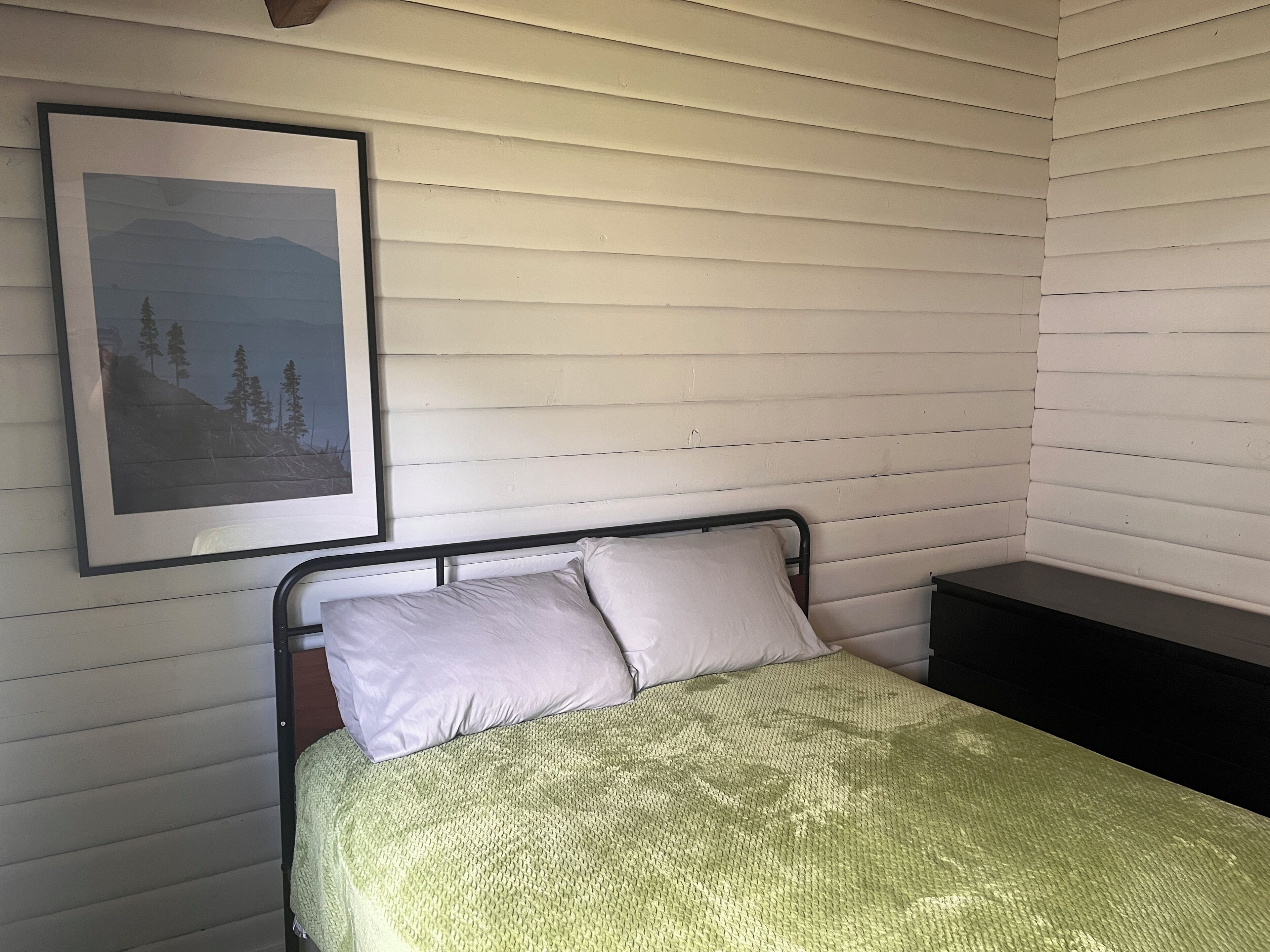 Une chambre à coucher avec un lit, des oreillers, une table de chevet et un tableau encadré au mur.