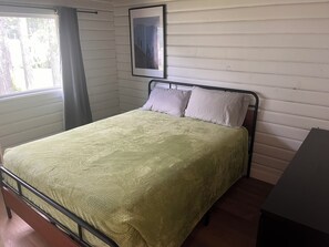 Un llit individual amb estructura metàl·lica, un edredó verd i dos almoinos. Al mur, sobre el llit, hi penja un quadre emmarcat.