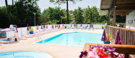 A swimming pool with lounge chairs and umbrellas, surrounded by trees and a wooden deck.