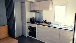 A compact kitchen with a built-in oven, a stovetop, and a window. - Mobilhome 2 chambres 2 SDB (Canet-en-Roussillon)