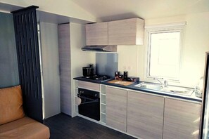 Eine kleine Küche mit Backofen, Kochfeld und Fenster.
