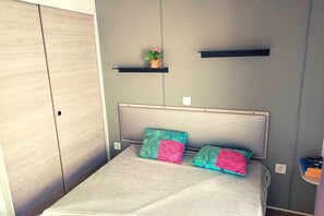 Ein Schlafzimmer mit einem Bett, zwei Kissen, einem Kopfteil, einem Kleiderschrank und einem Regal mit einer Pflanze.