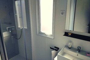 Ein Badezimmer mit Duschkabine aus Glas, einem Waschbecken mit Spiegel darüber und einem Fenster für natürliches Licht.