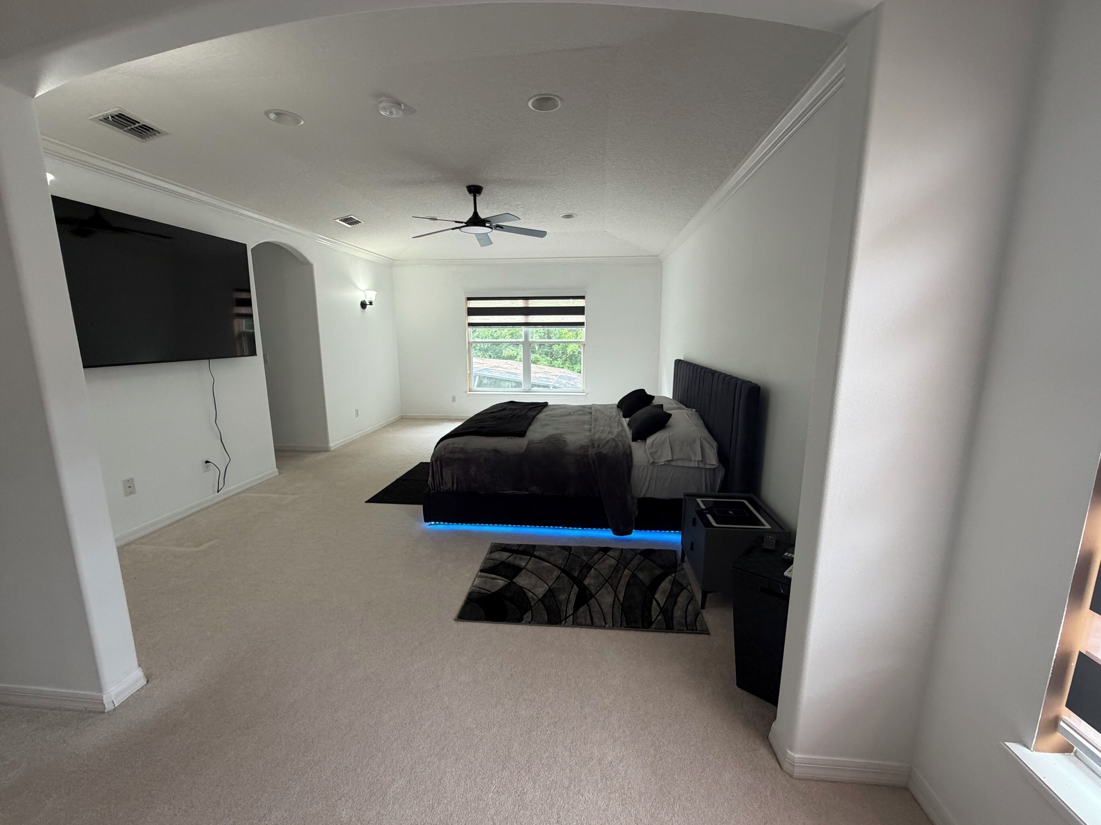 Une chambre à coucher avec un lit, un ventilateur de plafond, une télévision et une fenêtre.