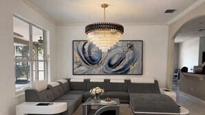 Un salon moderne avec un canapé d’angle, une table basse en verre et un grand tableau abstrait.
