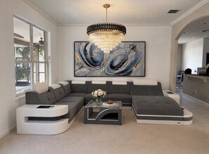 Een moderne woonkamer met een modulaire bank, een glazen salontafel en een groot abstract schilderij.