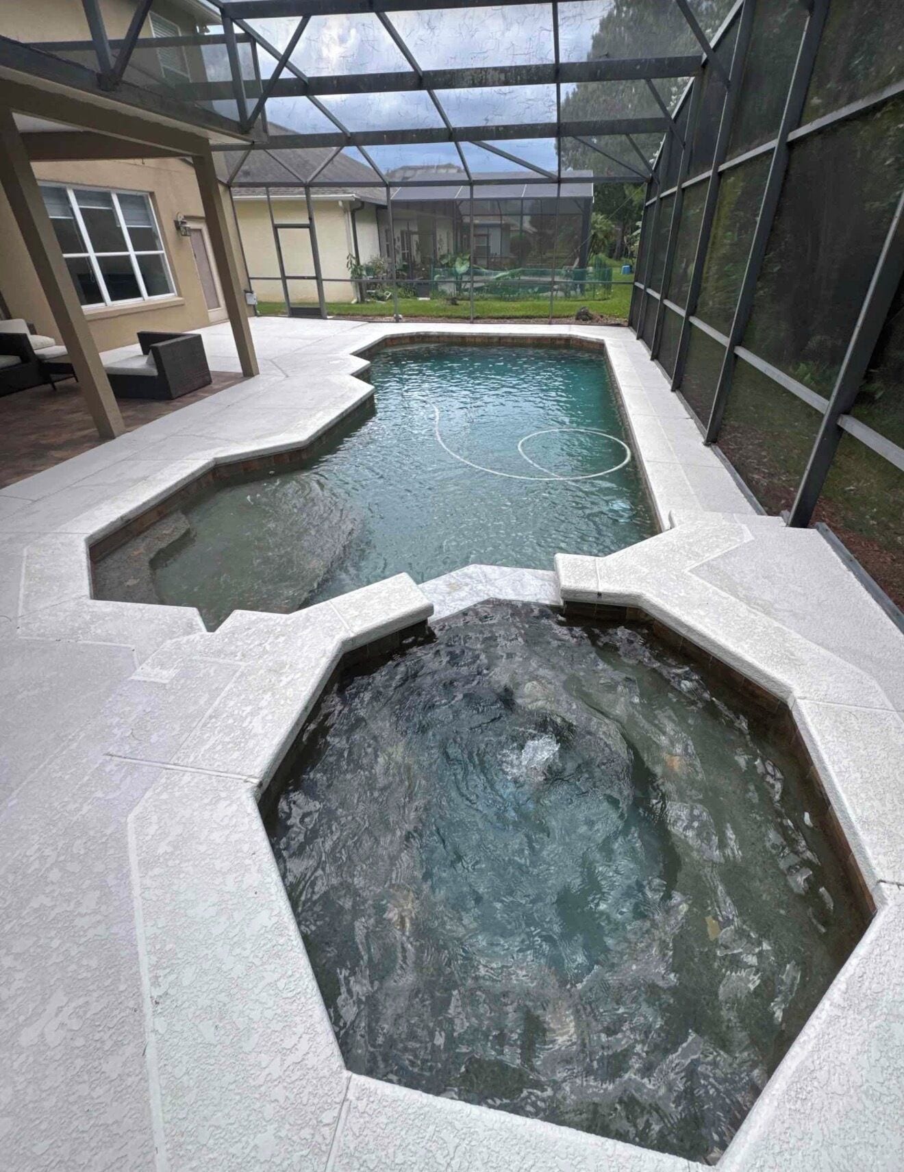 A swimming pool area with a glass enclosure, a hot tub, and a patio with seating.