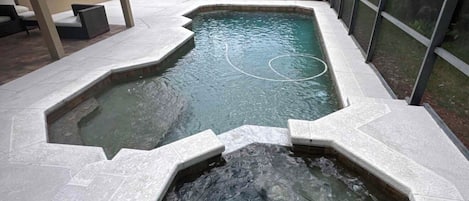 A swimming pool area with a glass enclosure, a hot tub, and a patio with seating.