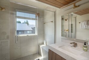 Un bagno moderno con cabina doccia in vetro, uno specchio grande e un lavabo in marmo.