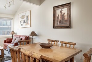 Un'area pranzo con un tavolo di legno, sedie e una ciotola. Alle pareti, due quadri.