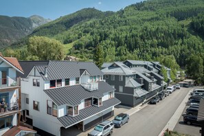 Quartiere residenziale con case moderne, una strada e montagne boscose sullo sfondo.