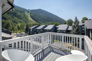 A balcony with white railings overlooking a row of modern buildings and a forested mountain. - Downtown Telluride Condo | Walk to Gondola | Mountain Views | Sleeps 6 (Telluride)
