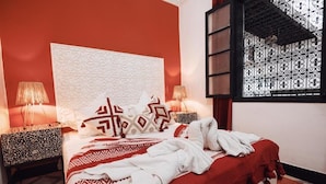 A bedroom with a large bed, patterned pillows, two bedside tables with lamps, and a window with decorative ironwork. - RIAD NEW MOON (Marrakech)