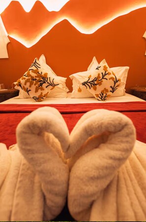 Una cama con almohadas blancas y una colcha roja, con un par de toallas dispuestas en forma de corazón.