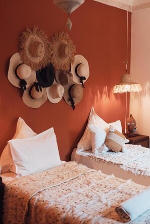 A room with two beds, a wall-mounted hat rack, a hanging lamp, and a small table with a lamp. - RIAD NEW MOON (Marrakech)