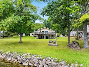 A two-story house with a balcony, surrounded by a well-maintained lawn and trees. - Loonar Landing: (Cheboygan)  Lakefront on Long Lake, Sleeps 8 (Cheboygan)