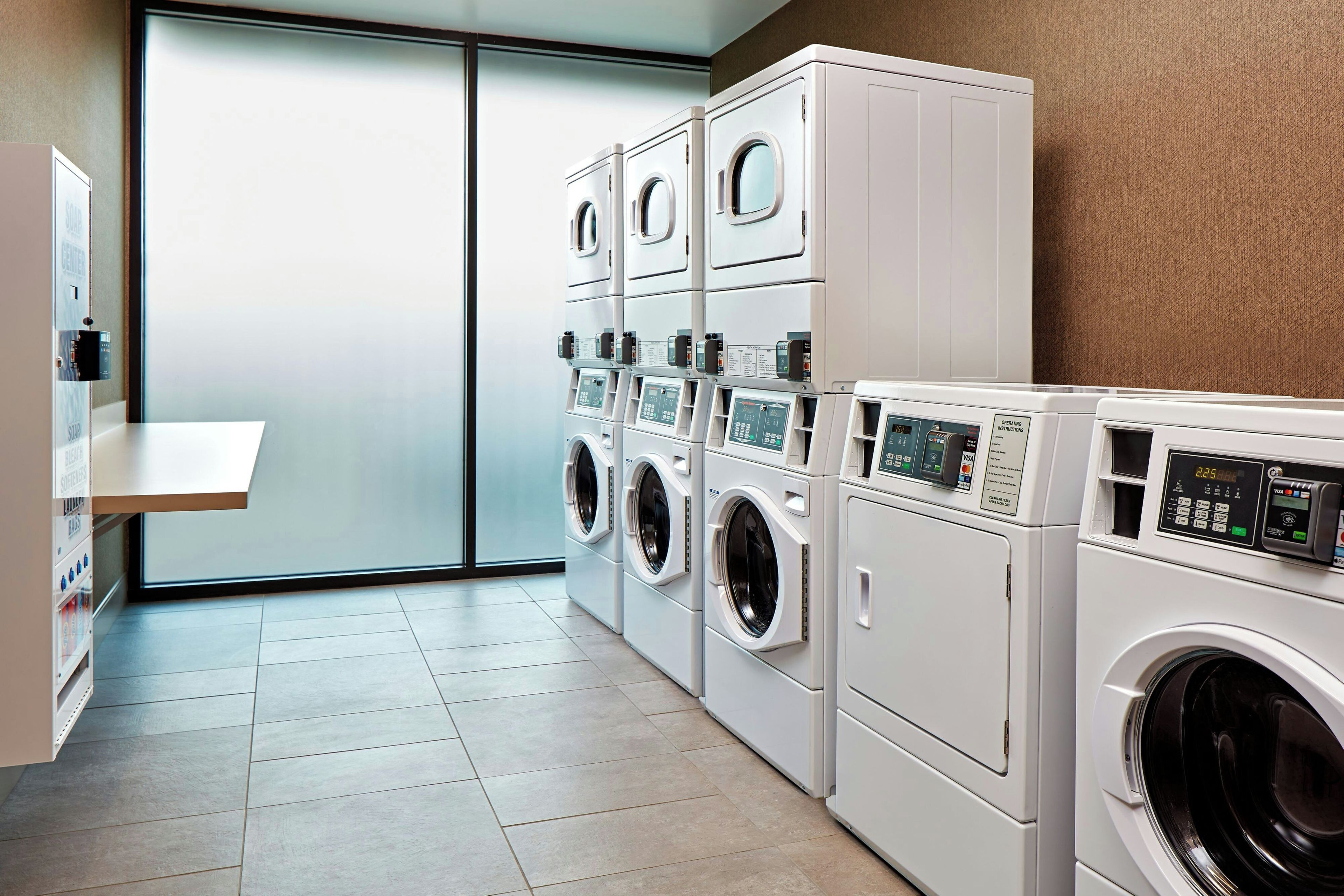A laundry room with multiple washing machines and dryers, a sink, and a glass door leading to an outdoor area.