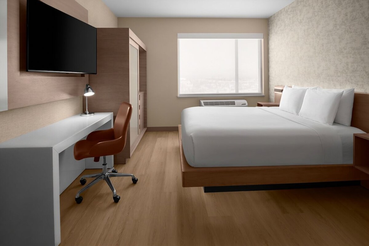 Habitación de hotel con cama, escritorio, silla, televisor y ventana.