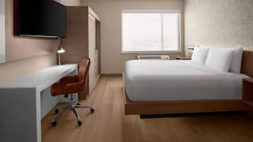 A hotel room with a bed, desk, chair, TV, and window.