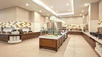 Ein modernes Buffet mit einer zentralen Servicestation, mehreren Essensauslagen und einem sauberen, gefliesten Boden.