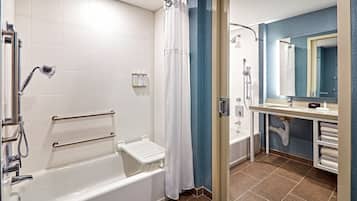 A modern bathroom with a walk-in shower, grab bars, a bathtub, and a vanity with a mirror.