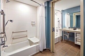 Un baño moderno con cabina de ducha, barras de apoyo, bañera y tocador con espejo.