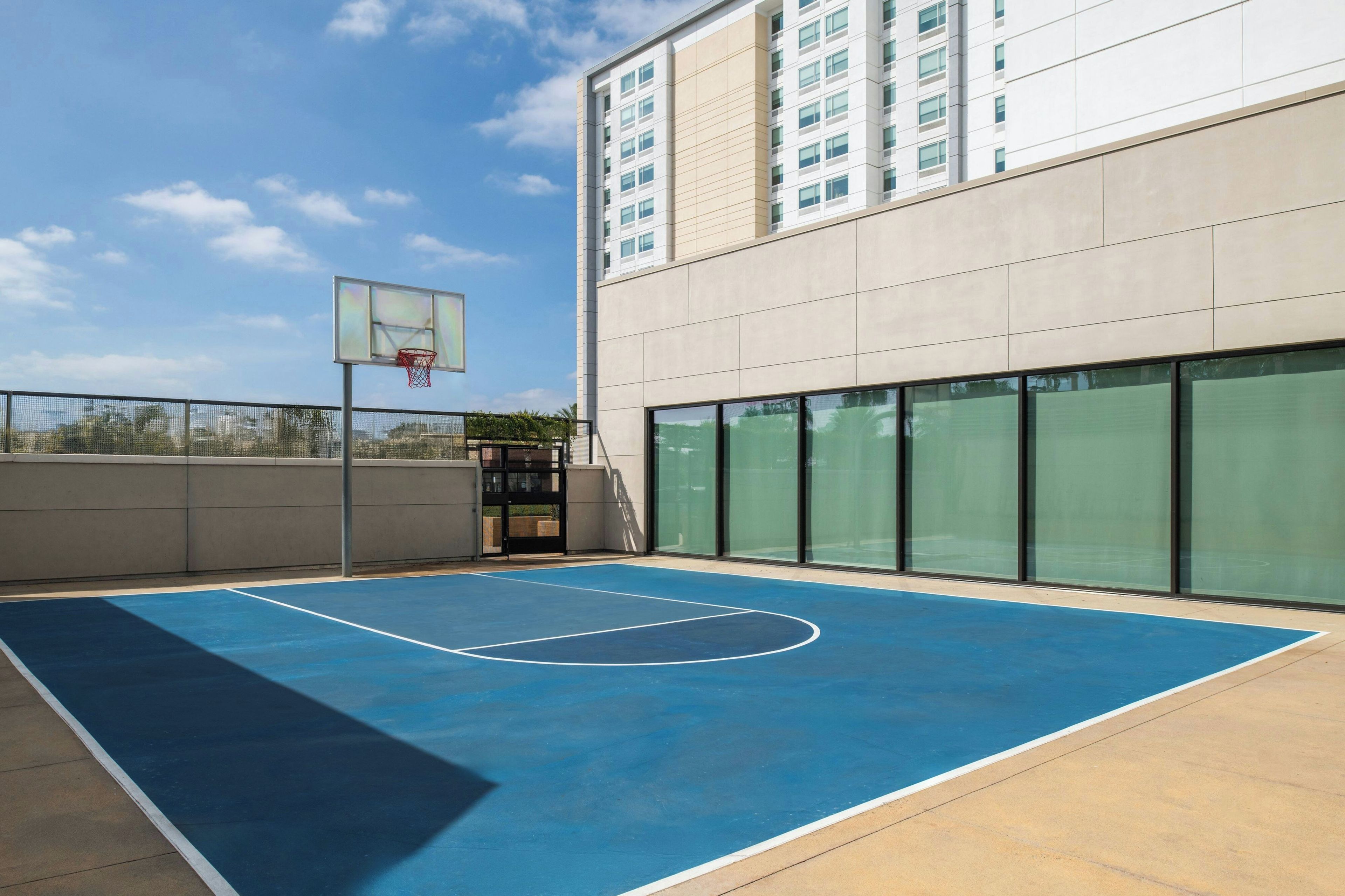 An outdoor basketball court adjacent to a building with large windows.