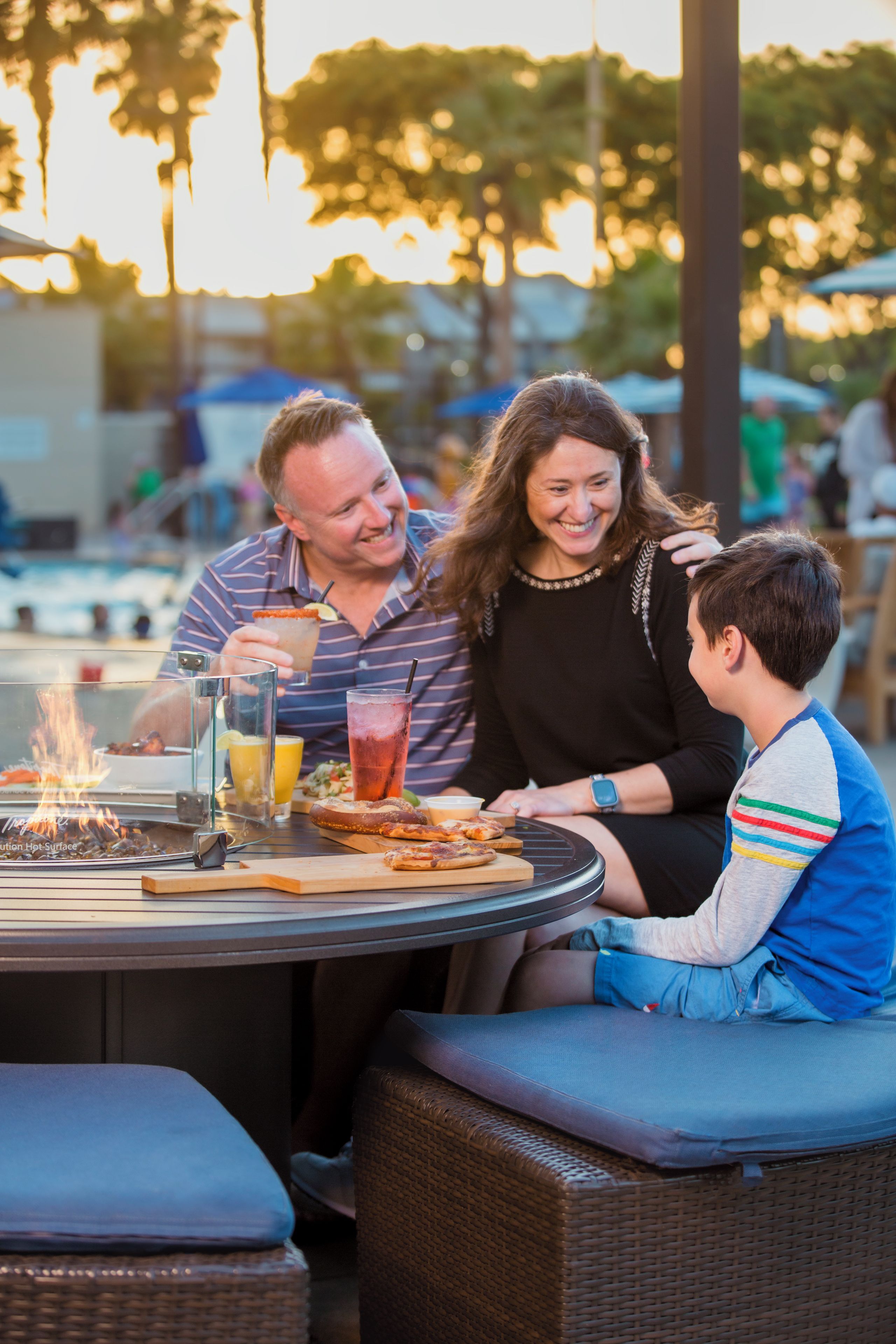 A dining table with a fire feature, drinks, and food.