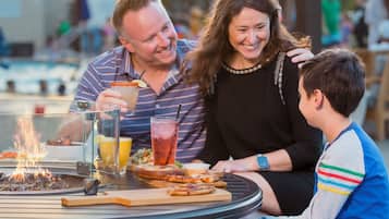 A dining table with a fire feature, drinks, and food.