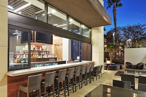 A bar area with a long counter, multiple seating options, and a view of the outdoor environment. - Springhill Suites By Marriott Anaheim Theme Park / Convention Area (Anaheim)