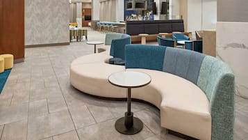A modern lounge area with a curved sofa, small round tables, and a bar area in the background.
