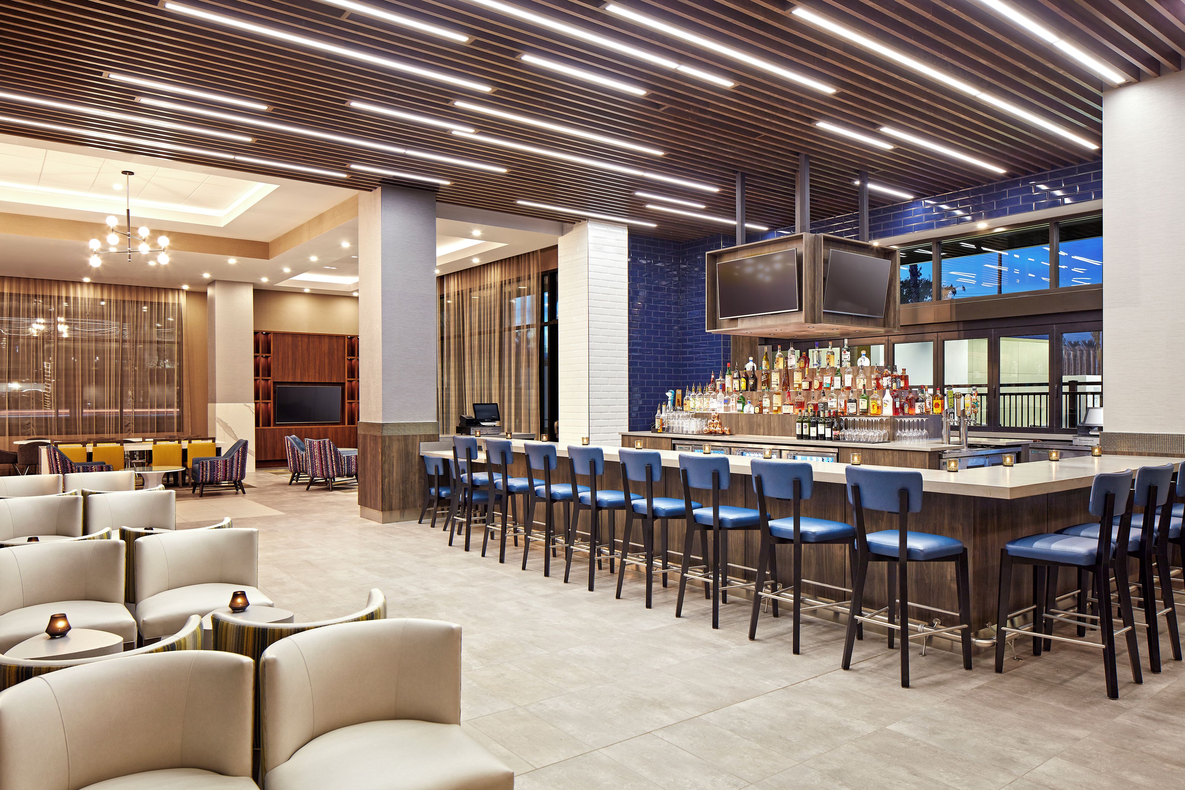 A modern bar area with a long counter, multiple bar stools, and a television screen.