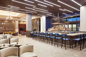 A modern bar area with a long counter, multiple bar stools, and a television screen.