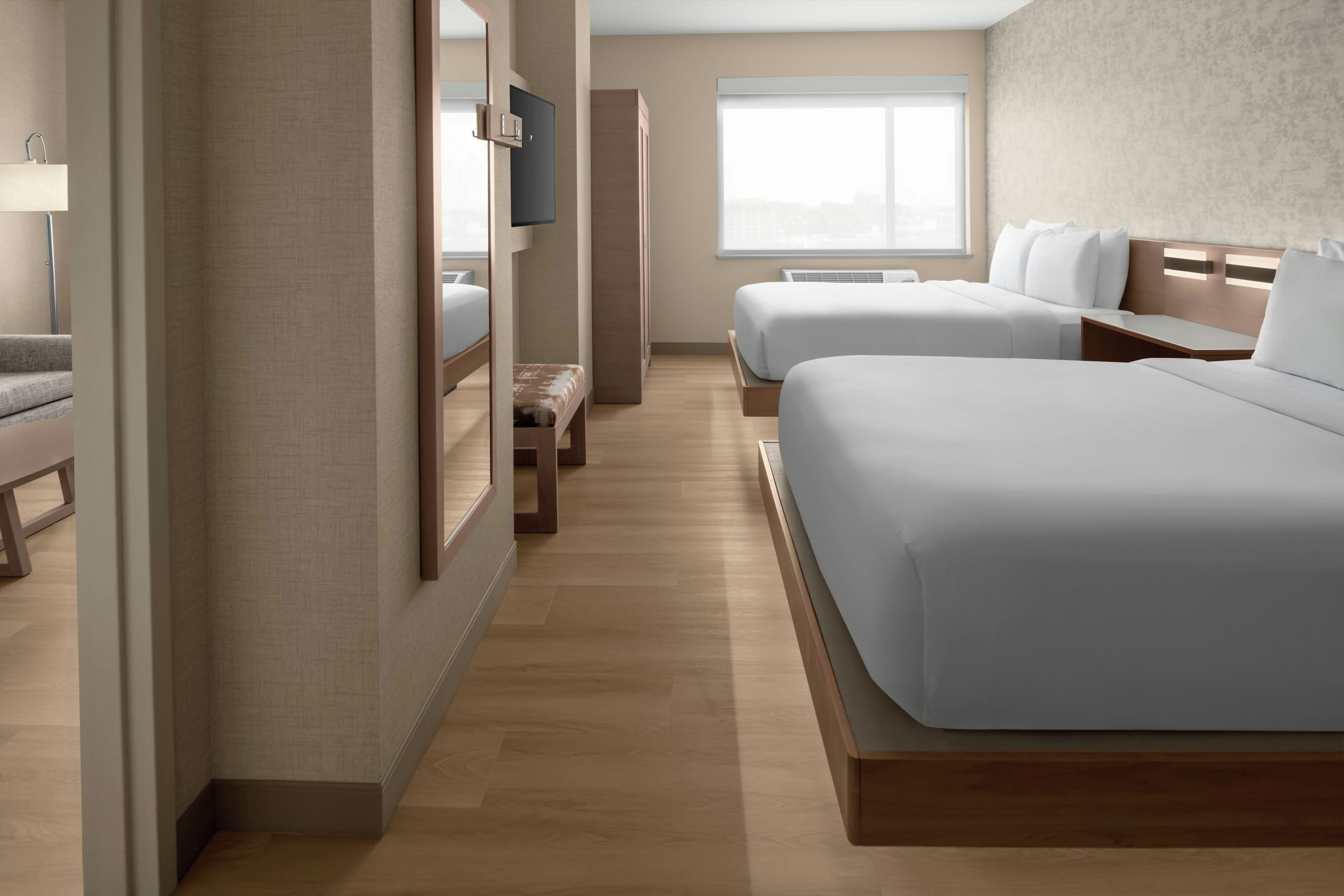 Quarto de hotel com duas camas, um sofá, uma televisão e janela com vista para a cidade.