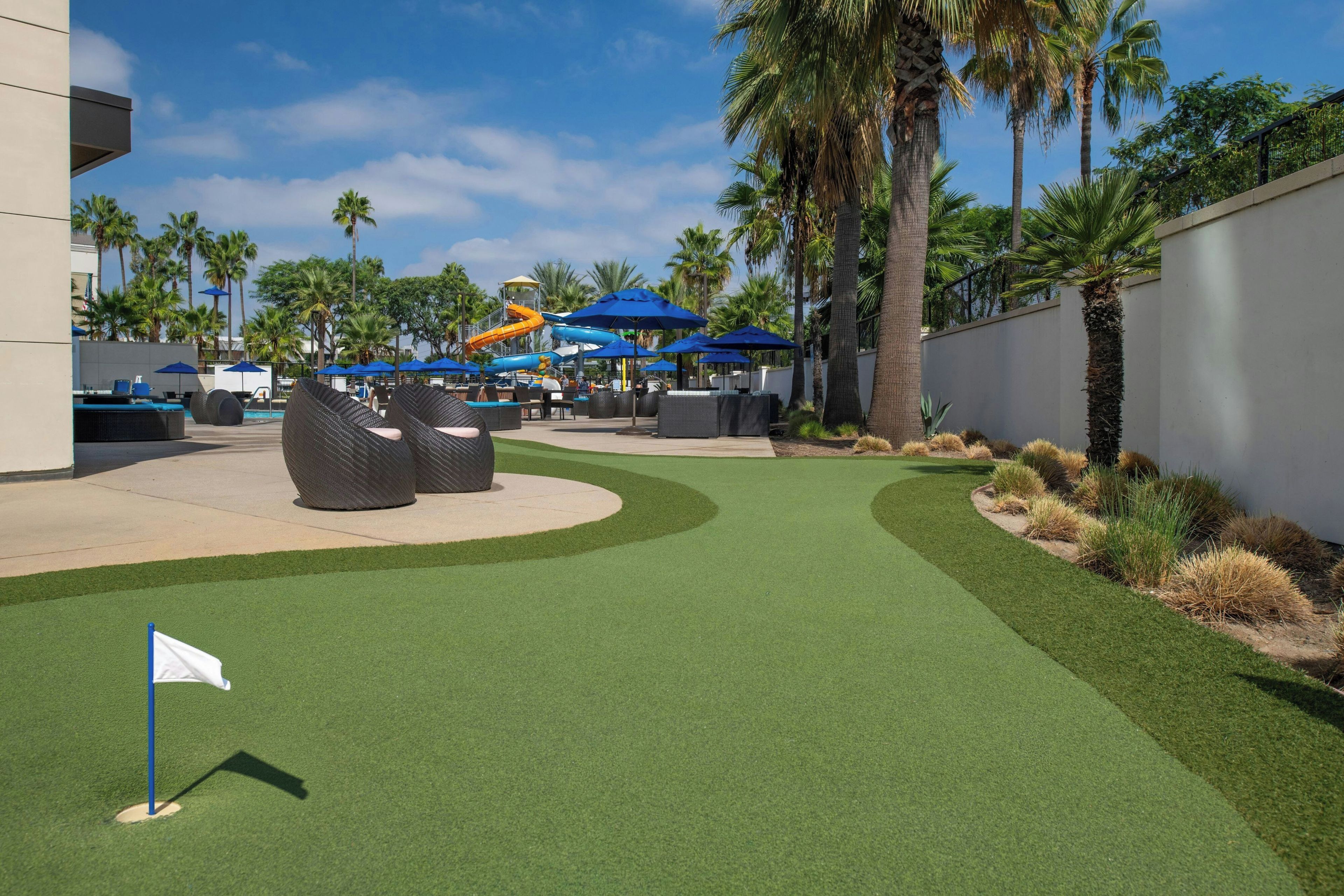 Un parcours de golf avec une pelouse artificielle, un drapeau et un parc aquatique en arrière-plan.