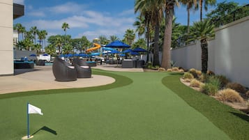 A golf course with artificial turf, a flag, and a water park in the background.