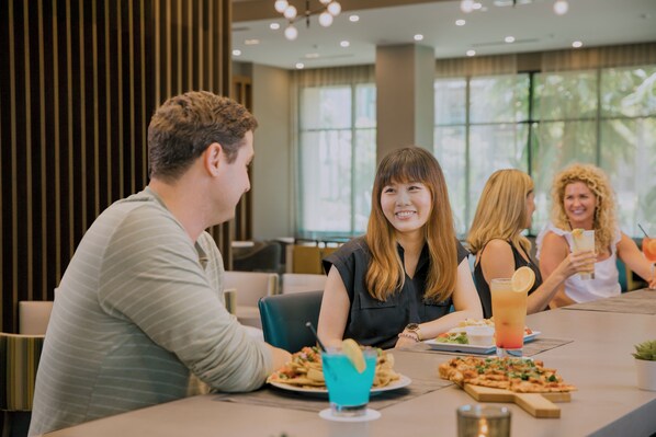A group of people dining at a restaurant with a modern interior, including a large window and a table with various dishes and drinks.