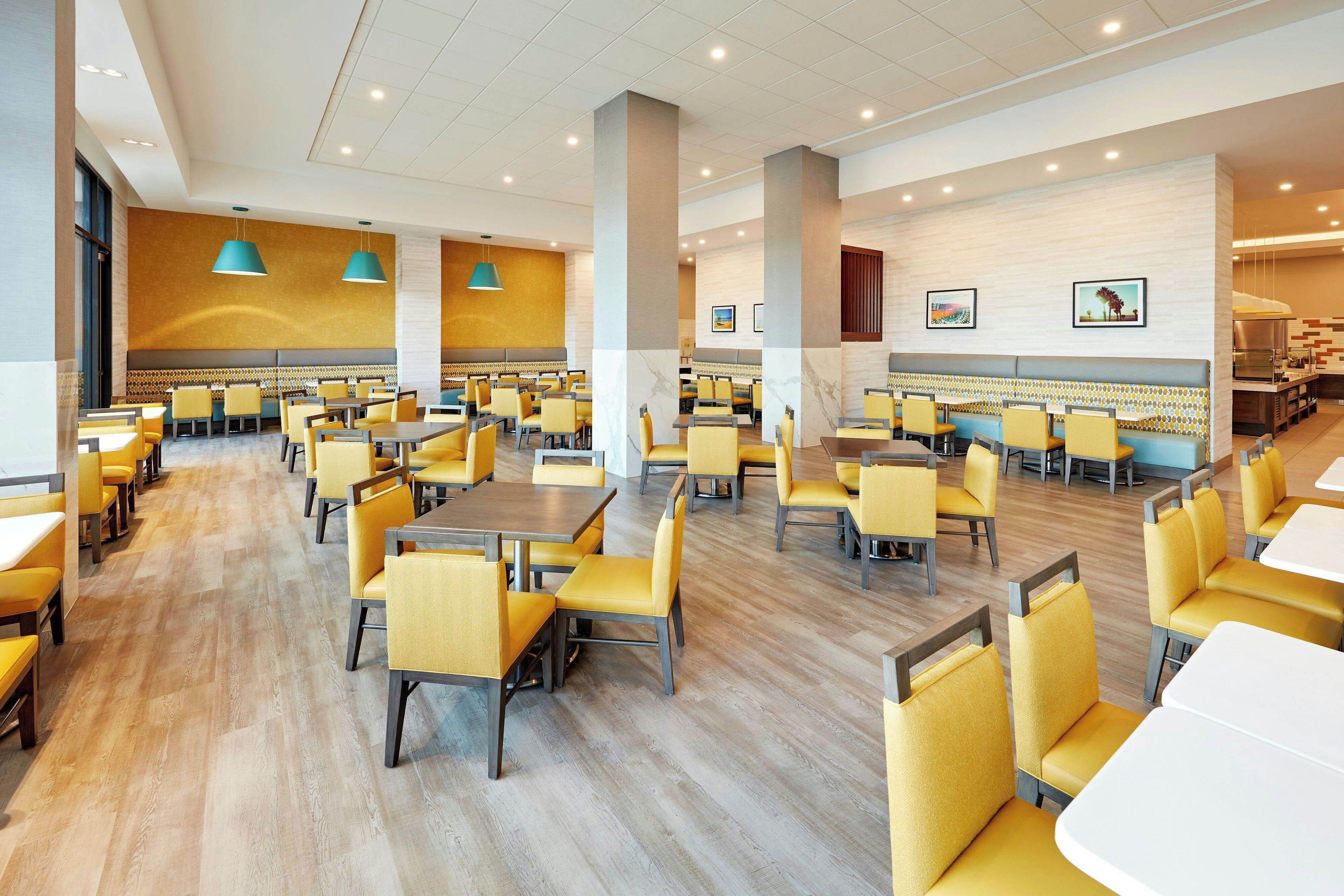 A spacious dining area with multiple tables and chairs, a kitchen area, and a seating area with a view of the outdoors.
