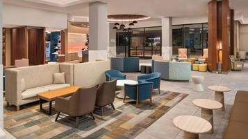 A modern lobby with seating areas, a coffee shop, and a view of the street.