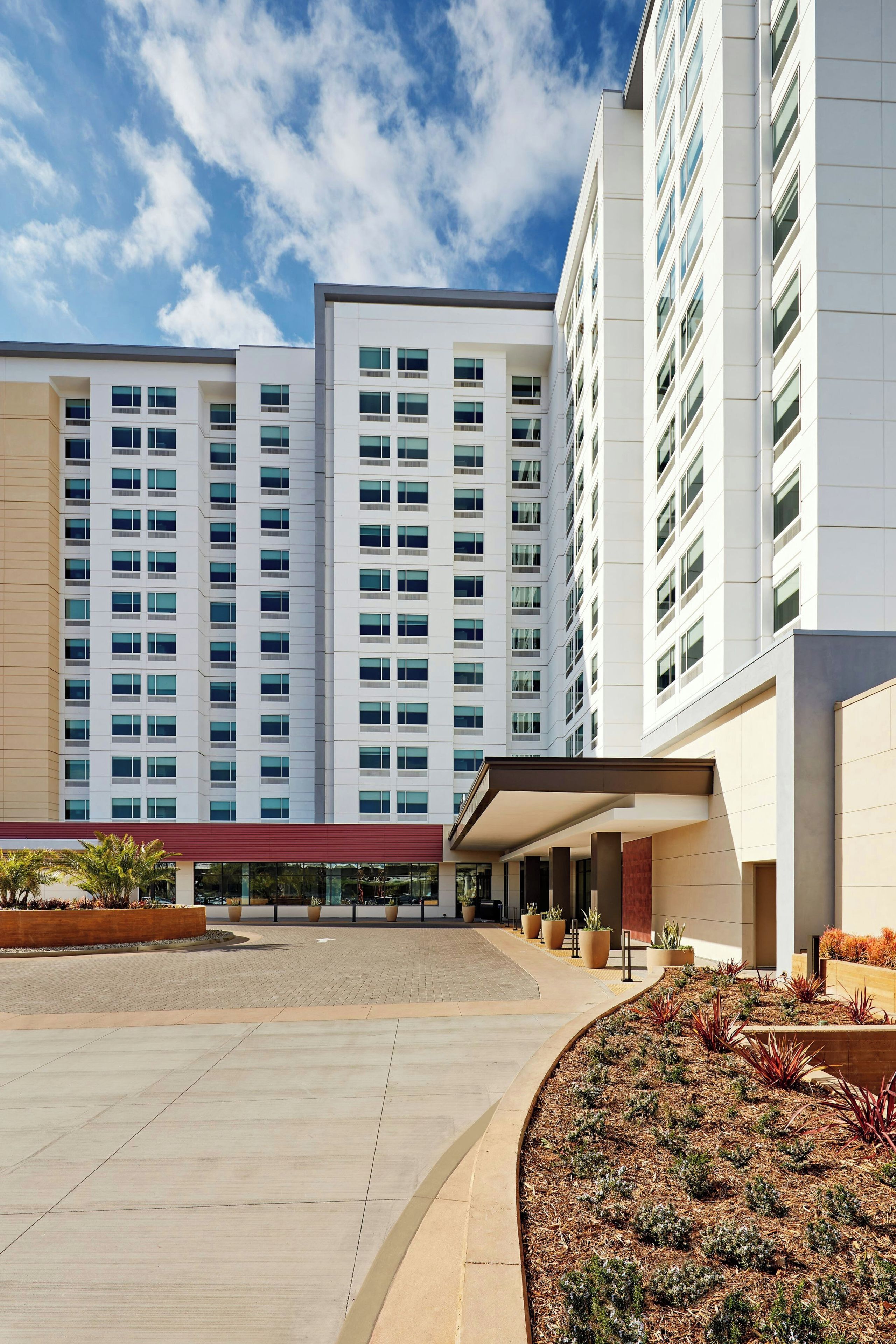 A modern building with multiple floors, large windows, and a covered entrance area with a landscaped garden.