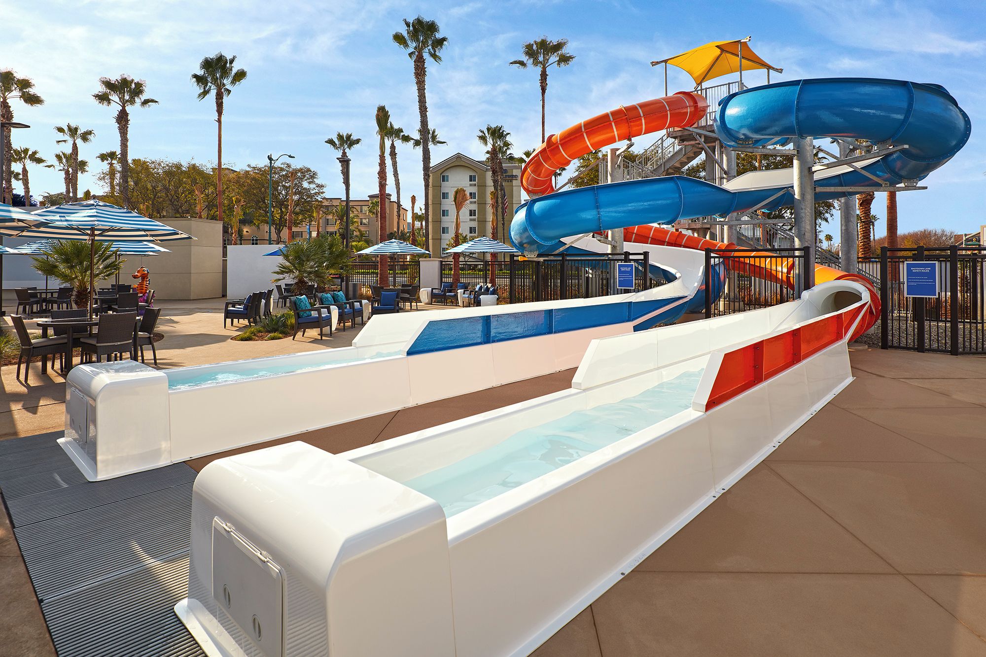 Ein Wasserpark mit mehreren Wasserrutschen und einem Poolbereich inklusive Liegestühle und Sonnenschirme.