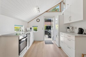 Moderni keittiö, jossa on valkoiset kaapit, sisäänrakennettu uuni ja kahvinkeitin.