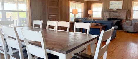 A dining area with a wooden table and white chairs, a blue sofa, and a fireplace with a stone mantle.