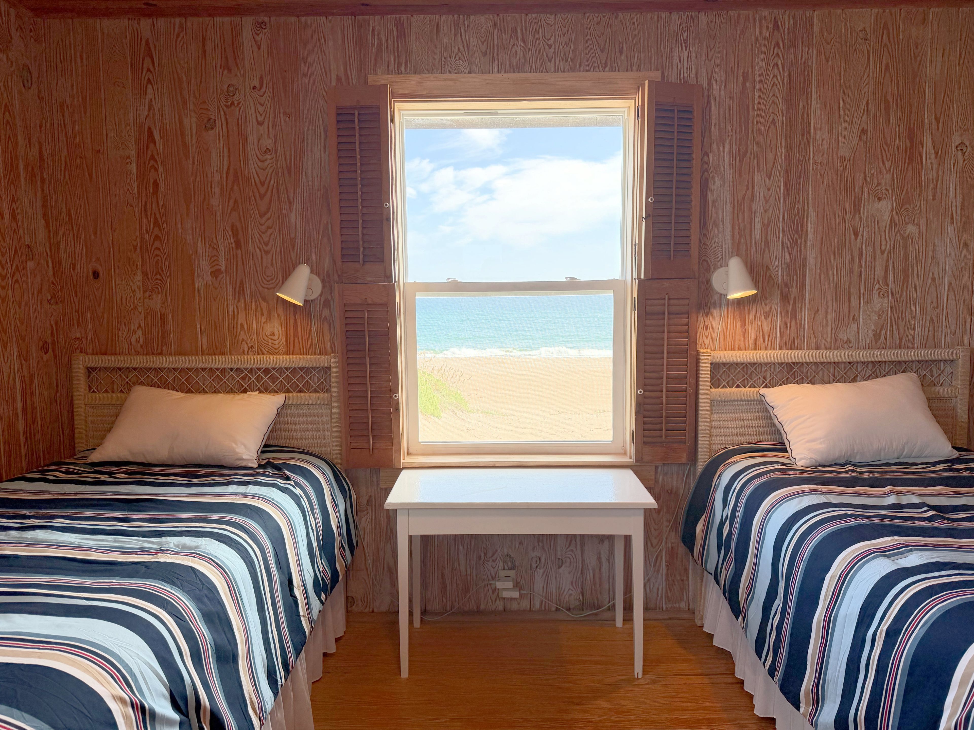 Ein Zimmer mit zwei Betten, einem kleinen Tisch und einem Fenster mit Blick auf den Strand.