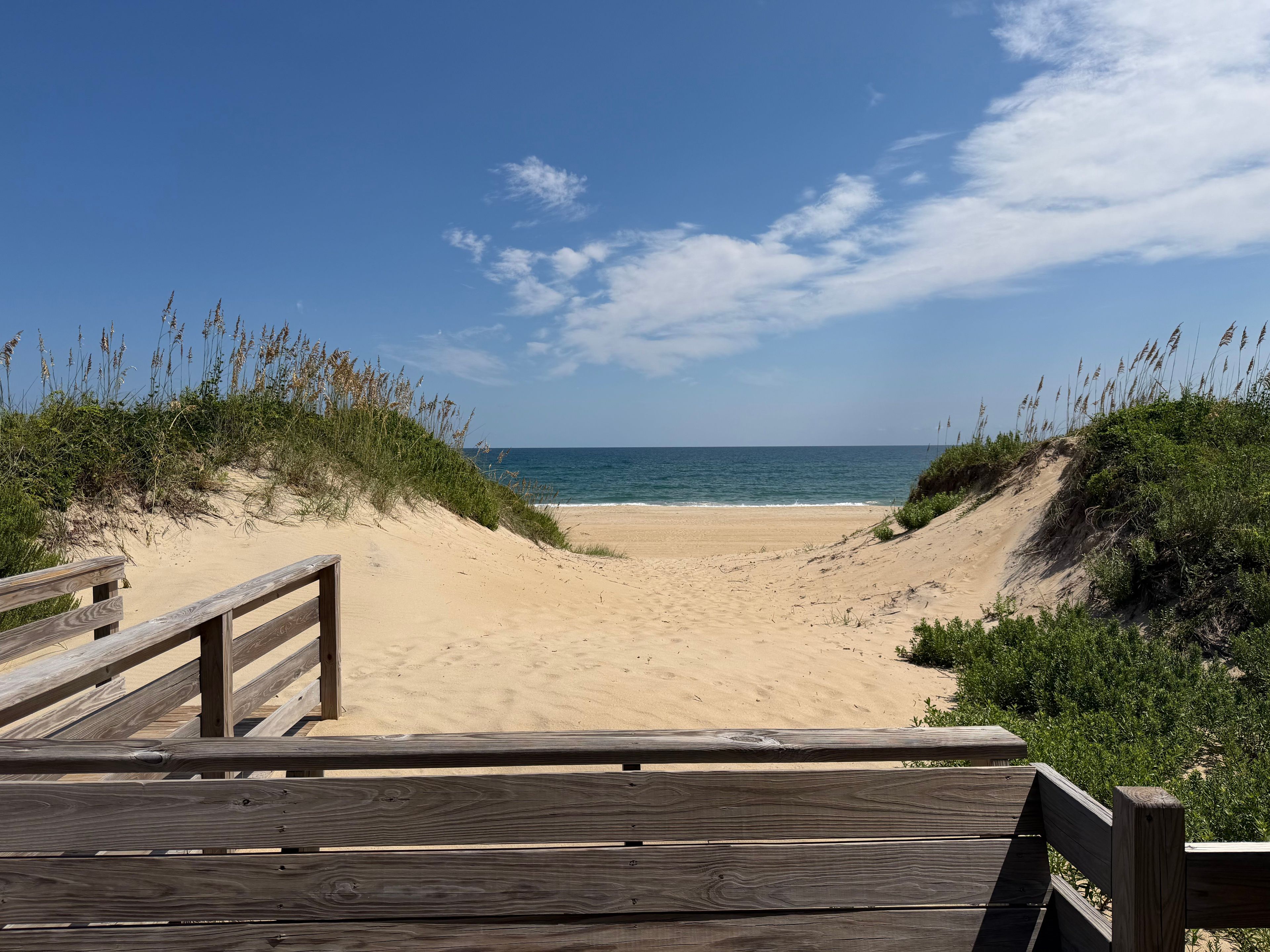 A wooden boardwalk leading to a sandy beach with dunes and vegetation.