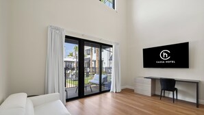 Ein modernes Hotelzimmer mit einer Schiebeglastür zu einem Außenbereich, einem Wand-Fernseher und Holzboden.