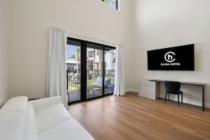 A modern hotel room with a sliding glass door leading to an outdoor area, a flat-screen TV mounted on the wall, and a wooden floor. - Cassa Hotel: Luxury Poolside 1BR/2BA Unit 101 (Orlando)